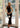 Woman in a black dress holding a white handbag indoors.